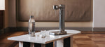 Carbonator 3 Steel with a matching water bottle and glass on a marble table in a stylish interior.