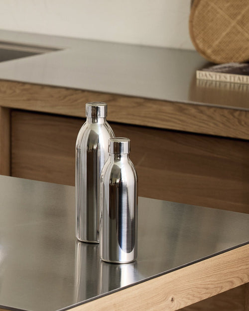 Aarke stainless steel To-Go Bottles in two sizes, Small and Large, standing side by side on a stainless steel kitchen countertop with wooden cabinetry in the background.
