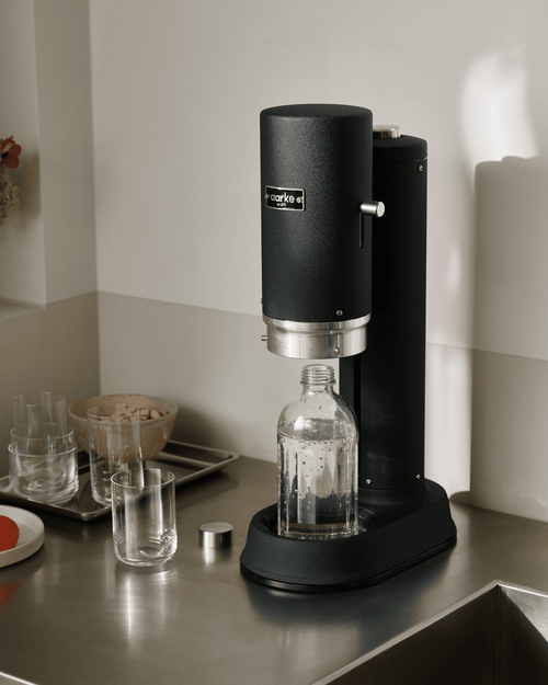 Aarke Carbonator Pro sparkling water maker in Matte Black with glass bottle on a stainless steel kitchen countertop.