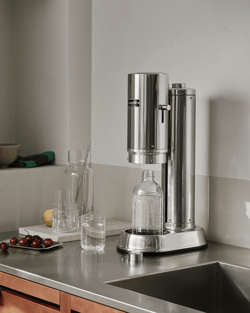 Aarke Carbonator Pro sparkling water maker in Stainless Steel with glass bottle filled with sparkling water on a modern kitchen countertop.
