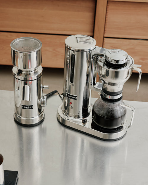 Aarke Coffee Grinder and Coffee Maker in polished stainless steel connected via AutoGrind™, with freshly brewed coffee in the glass carafe.