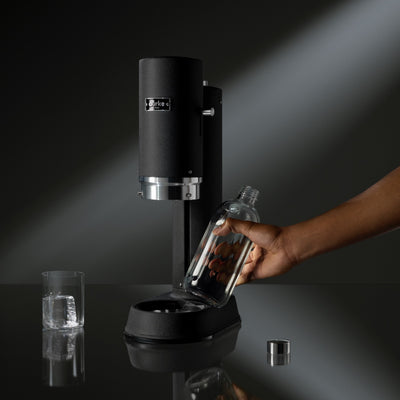 Hand placing glass bottle into black Aarke Carbonator Pro in Matte black for sparkling water preparation.