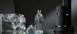 Sparkling water served in a premium Aarke glass bottle next to a black Aarke Carbonator Pro in Matte black and sculpted ice block on a sleek dark surface.