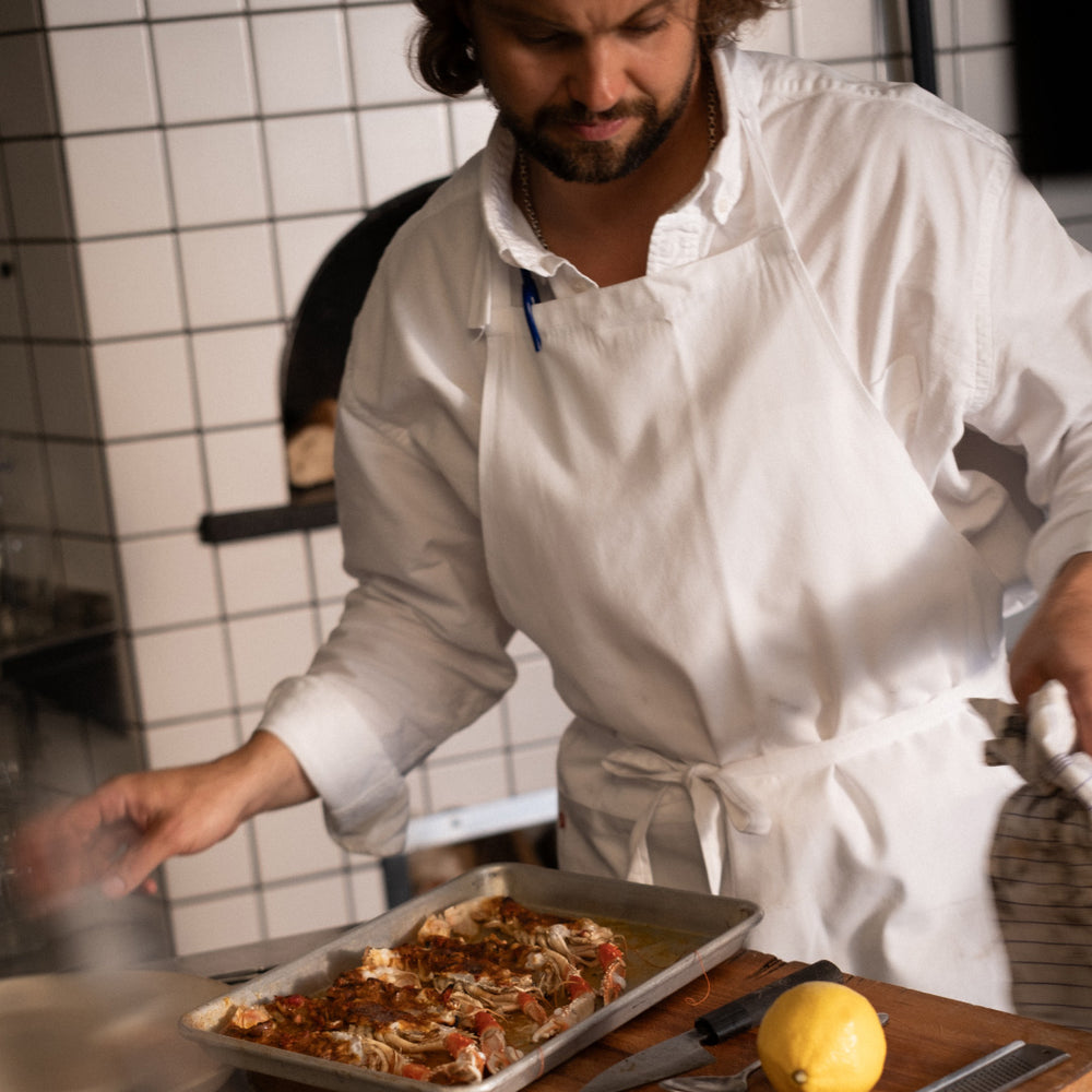 Person in a kitchen preparing food with a tray of seafood and a lemon on a cutting board.