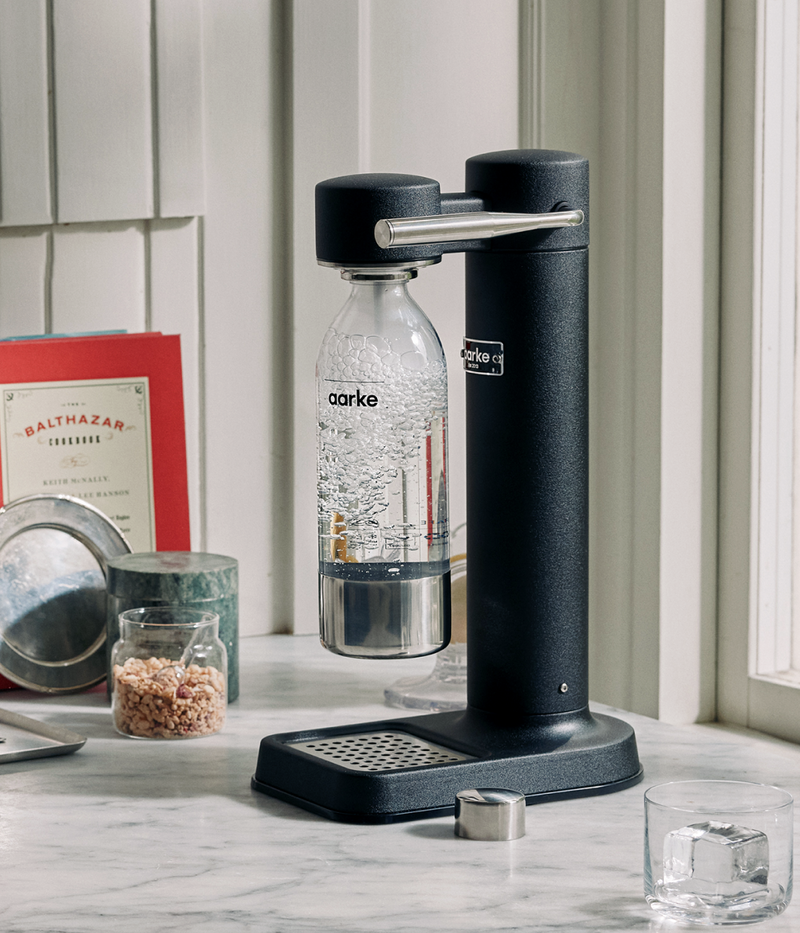 Aarke Carbonator 3 in matte black on a marble countertop, carbonating water in an Aarke PET bottle.