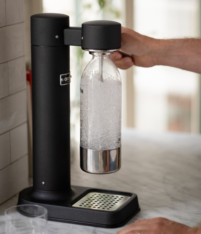 Person pressing the lever on the Aarke Carbonator 3 in matte black, carbonating water in an Aarke PET bottle.
