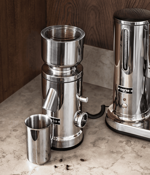 Aarke Coffee Grinder placed on a kitchen counter with the coffee container beside it, next to an Aarke Coffee Maker.