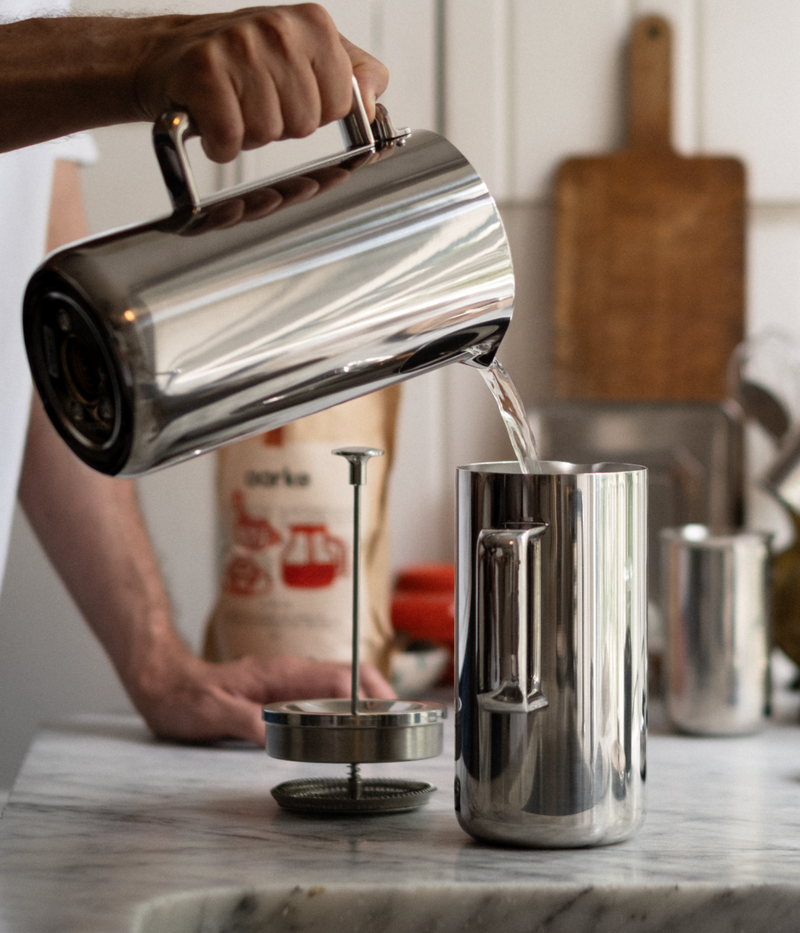 Person pouring hot water into Aarke stainless steel French Press using the Aarke Kettle.
