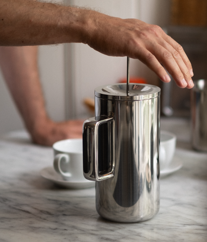 Hand pressing Aarke stainless steel French Press plunger on marble countertop.