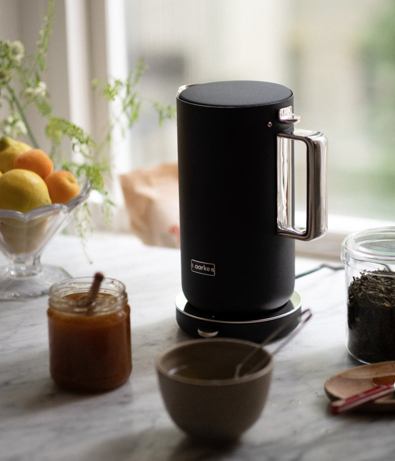 Aarke matte black electric kettle on a kitchen counter with a jar of honey, tea leaves, and a bowl ready for tea.