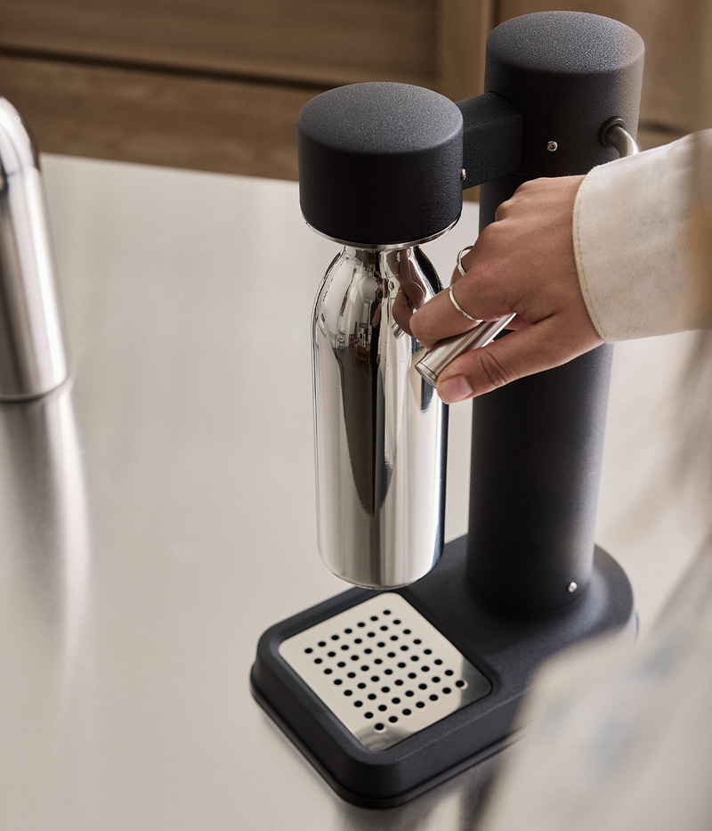 Person using the Aarke Carbonator 3 in matte black with a stainless steel Aarke to-go bottle small attached.