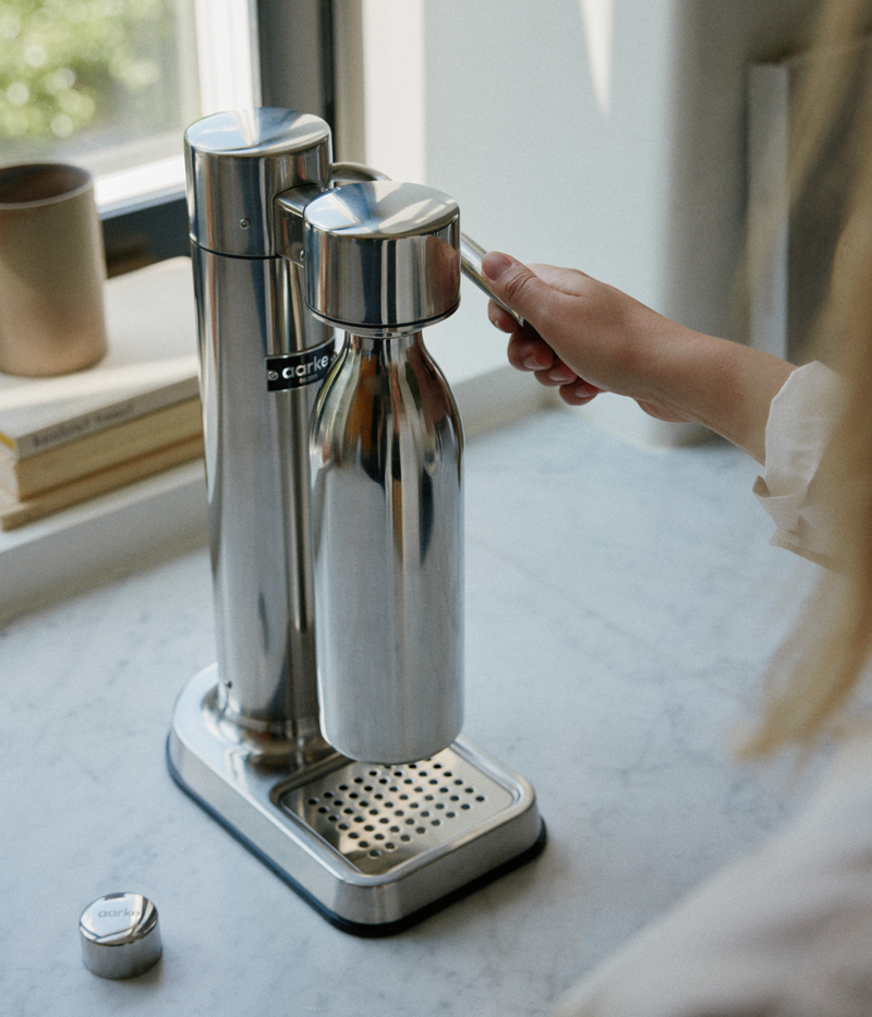 Close-up of a person carbonating water with the Aarke Carbonator 3 in stainless steel using the Aarke to-go bottle.