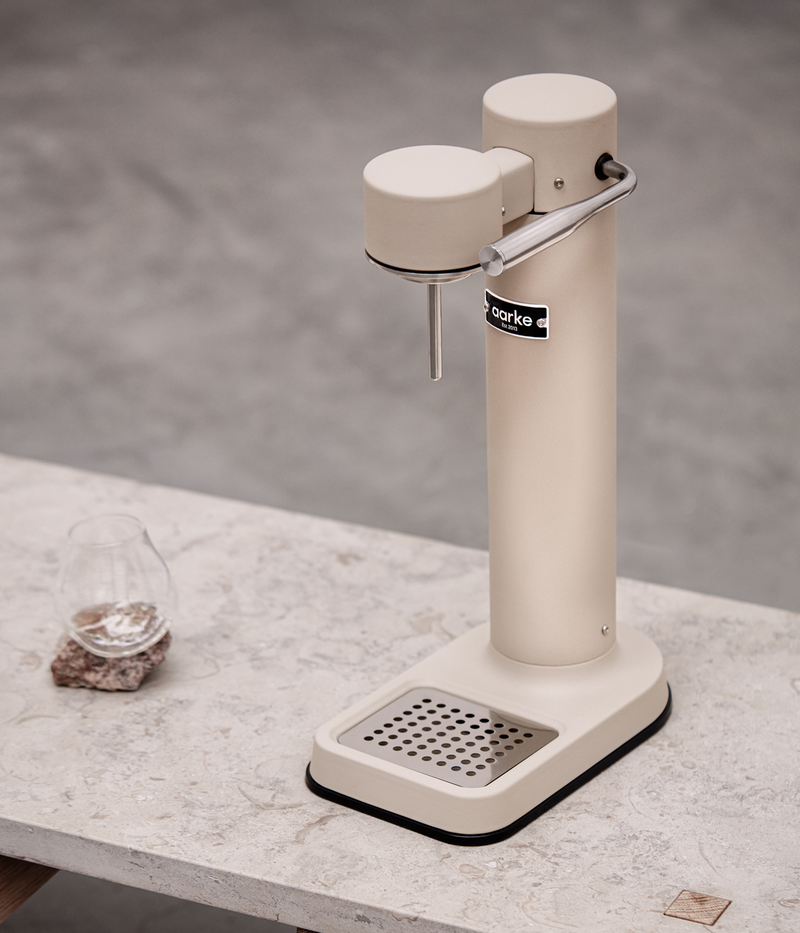 Aarke Carbonator 3 in sand finish on a stone table with a glass of sparkling water.
