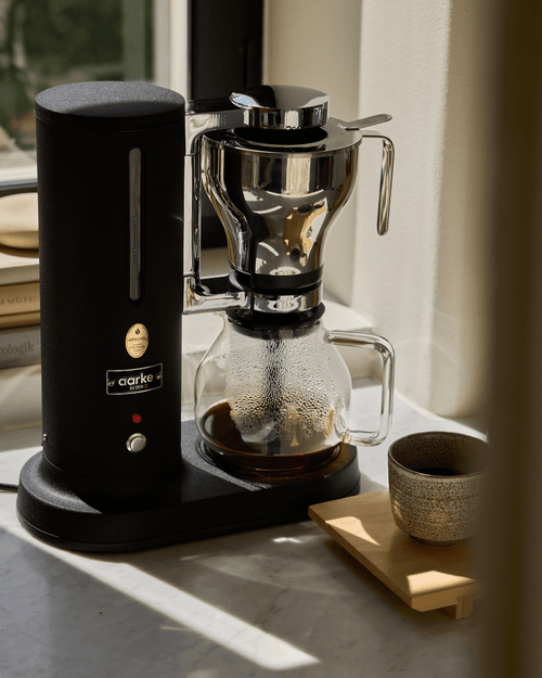 Aarke Coffee Maker in Matte Black with stainless steel filter basket and glass carafe containing freshly brewed coffee.