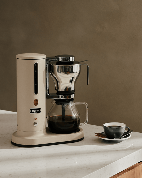 Aarke Coffee Maker in Sand with glass carafe filled with freshly brewed filter coffee, displayed on a kitchen countertop.