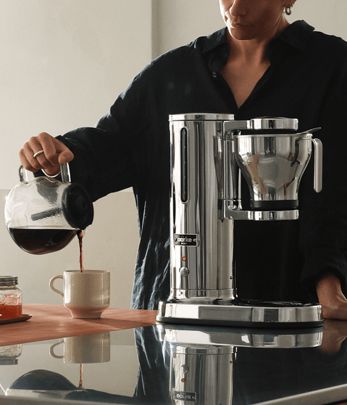 Aarke Coffee Maker in stainless steel with glass carafe, pouring freshly brewed filter coffee
