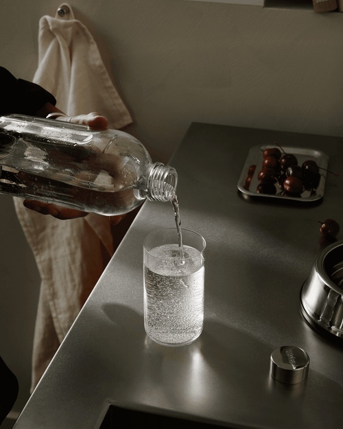 Sparkling water being poured from the Aarke Carbonator Pro glass bottle into a drinking glass on a kitchen countertop.