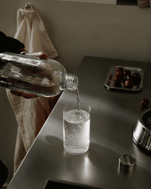 Sparkling water being poured from the Aarke Carbonator Pro glass bottle into a drinking glass.