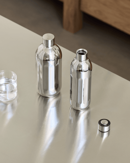 Two Aarke stainless steel To-Go Bottles in different sizes on a kitchen countertop, one with its cap removed.