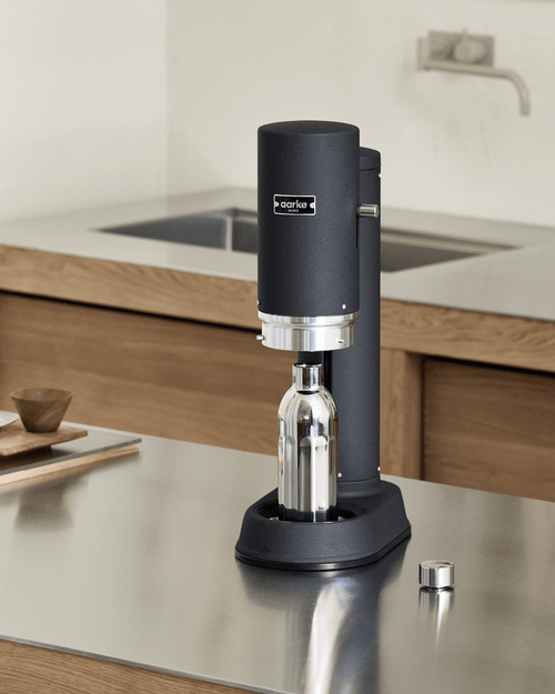 Aarke Carbonator Pro in Matte Black with a stainless steel To-Go Bottle Small, placed on a kitchen countertop with the bottle positioned inside the carbonator.