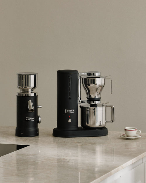 Aarke Coffee Grinder and Coffee Maker in Matte Black with stainless steel Thermal Jug on a marble kitchen countertop.