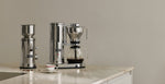Aarke stainless steel coffee maker and grinder on a stone countertop with freshly brewed filter coffee.