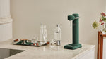 Aarke Carbonator 3 sparkling water maker in Heritage Green with Aarke BPA-free PET bottle and freshly carbonated sparkling water.