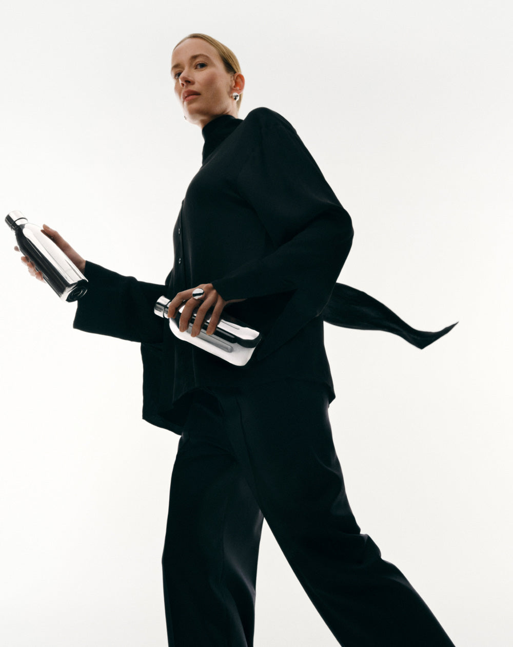 Person wearing a black outfit holding two aarke to-go stainless steel bottles against a white background