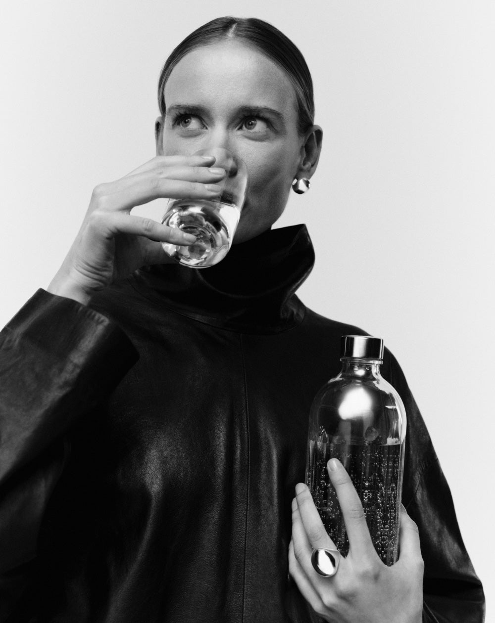 Person holding an aarke nesting glass and a aarke glass bottle, wearing a dark outfit against a white background