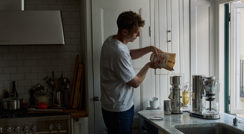 Man pouring from a container into a blender in a kitchen.
