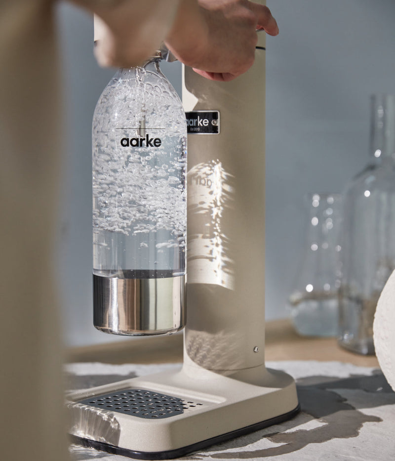 Close-up of the Aarke Carbonator 3 in Sand during carbonation, with bubbles rising in the attached PET bottle.