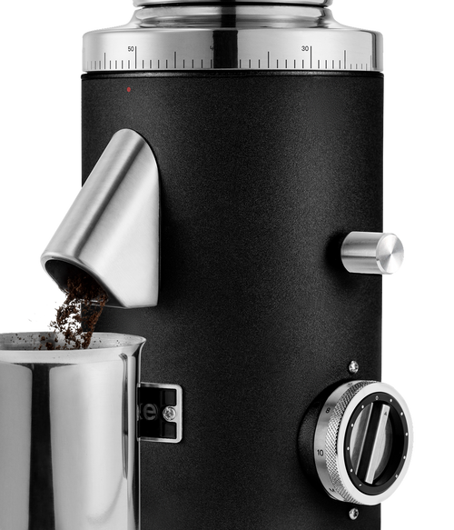 Close-up of the Aarke Coffee Grinder in Matte Black dispensing freshly ground coffee through the anti-static chute into the stainless steel coffee grounds cup.