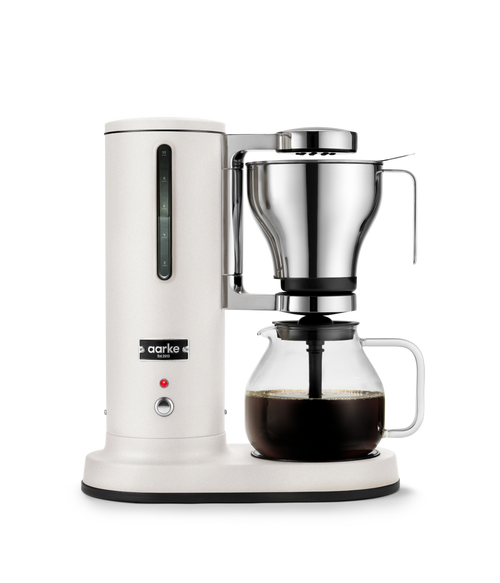Aarke matte white automatic pour-over coffee maker with stainless steel filter brewing coffee into glass carafe.