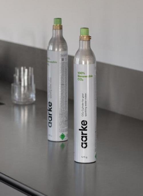 Two Aarke CO2 cylinders standing on a sleek stainless steel kitchen countertop, with glasses in the background